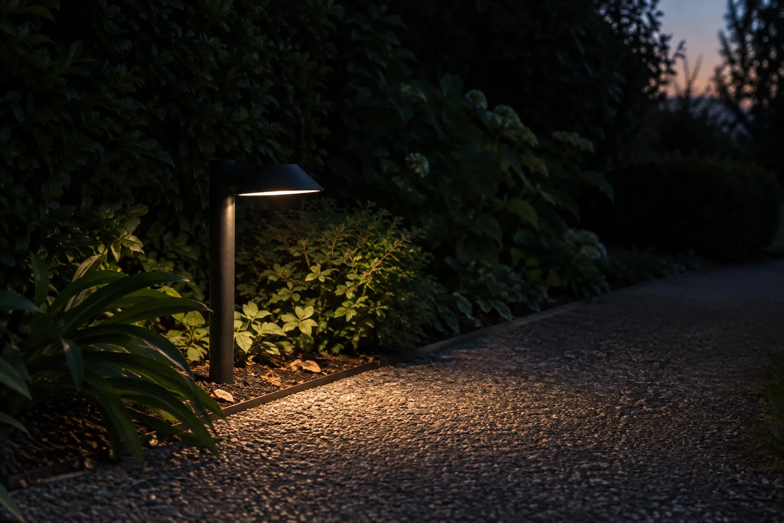 Une lampe munie d’un abat-jour éclaire un chemin sans diriger sa lumière vers la haie voisine.