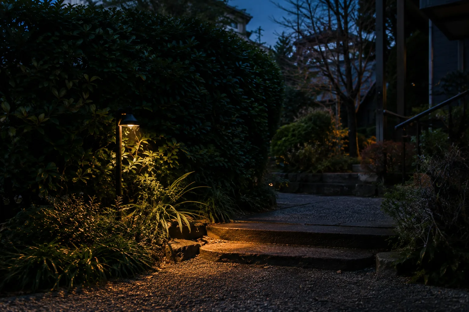 Une petite lampe extérieure éclaire un chemin sans illuminer la haie voisine.